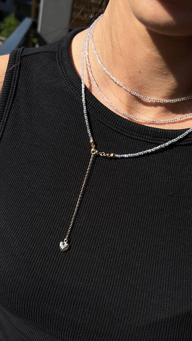 Trīs kārtu balts choker ar sirds piekariņu, elegants un stilīgs aksesuārs.