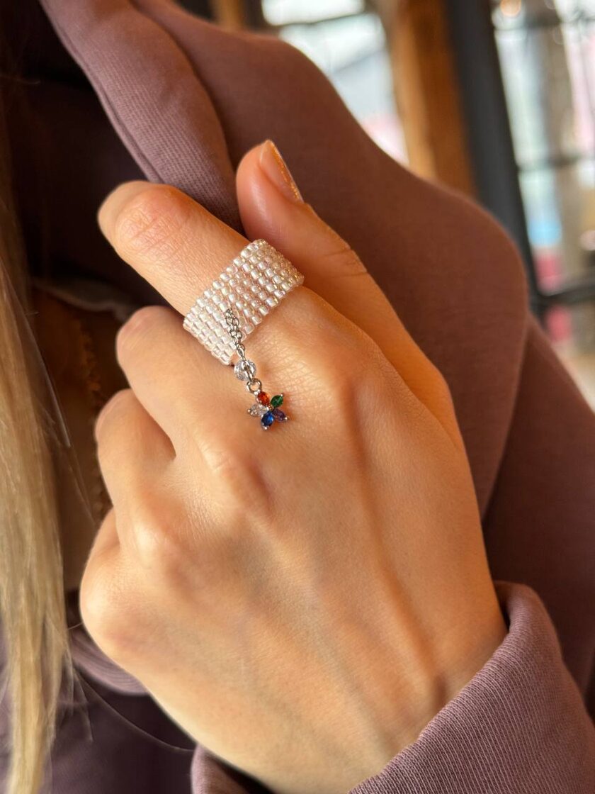 Balts pērļu rotas elements ar akmeni un krāsainu ziedu dekorāciju.