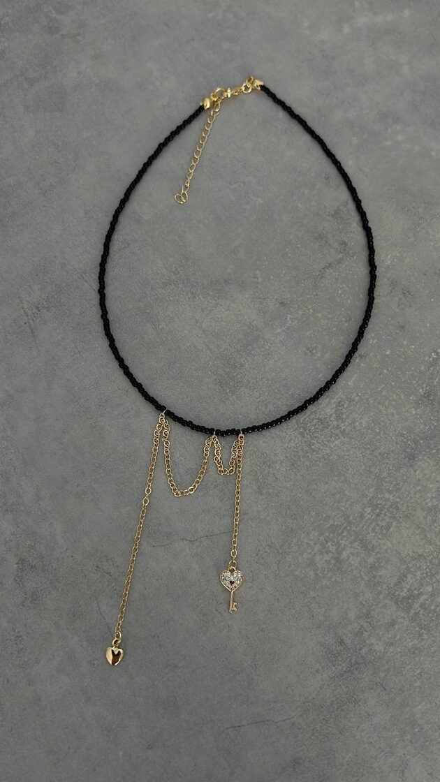 Melns choker ar atslēgu un mazu sirdi, elegants aksesuārs ikdienas apģērbam.