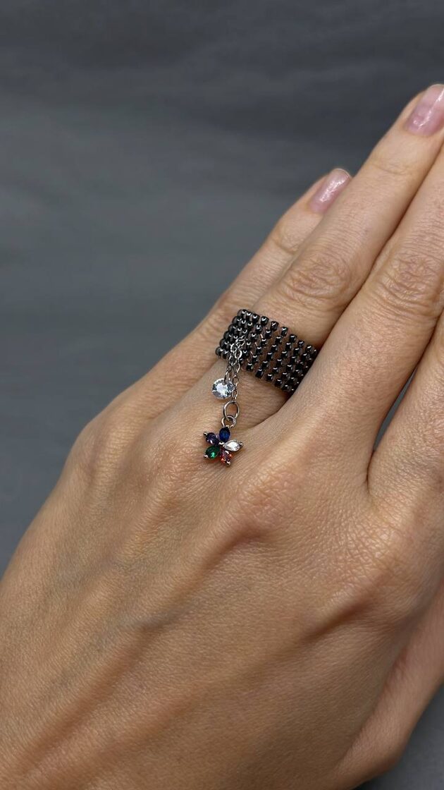 Grafīta krāsas rotaslieta ar ziedu zīmējumu un mazu akmeni.